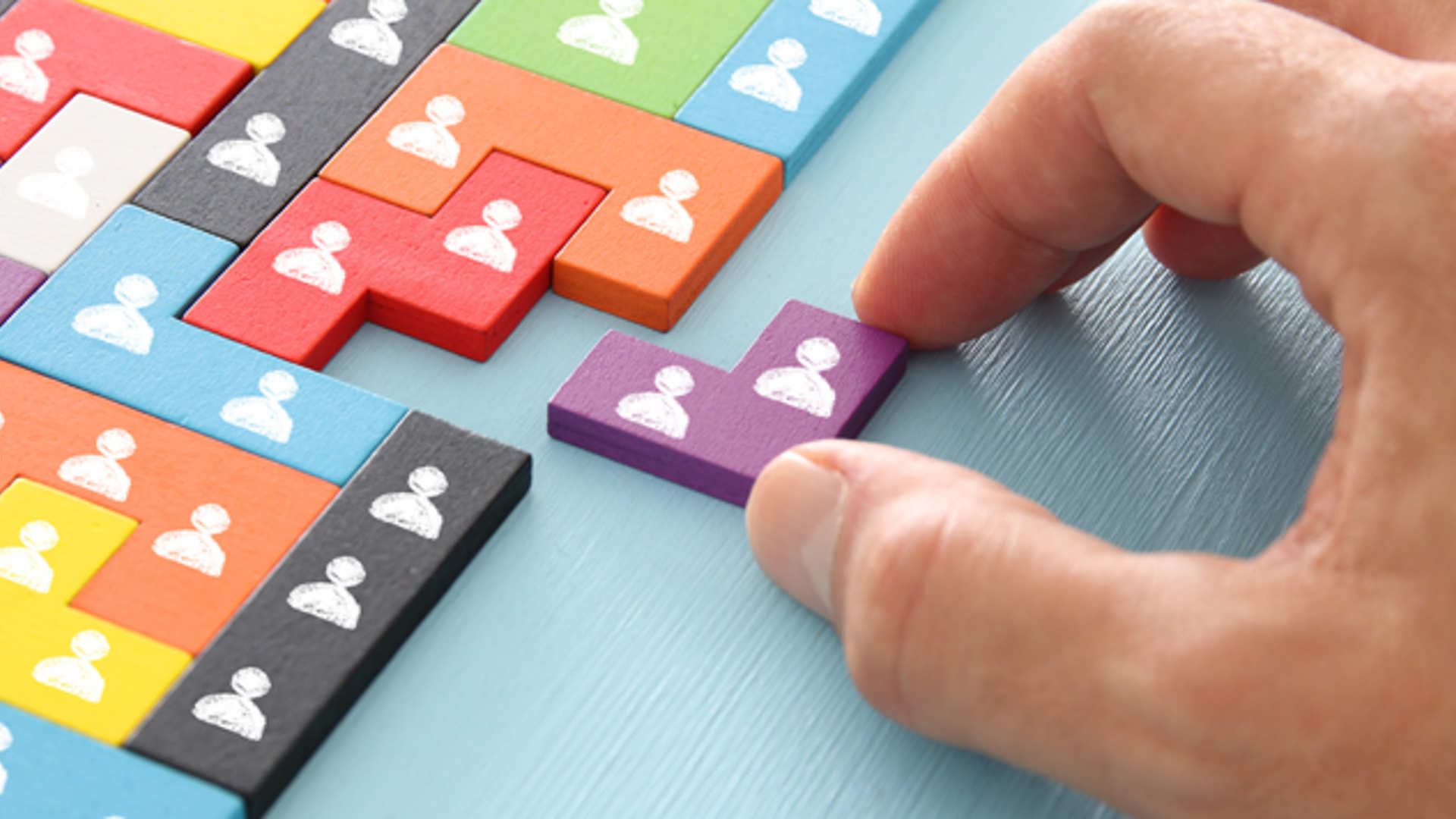 A hand places the final missing piece of a puzzle featuring symbols of people