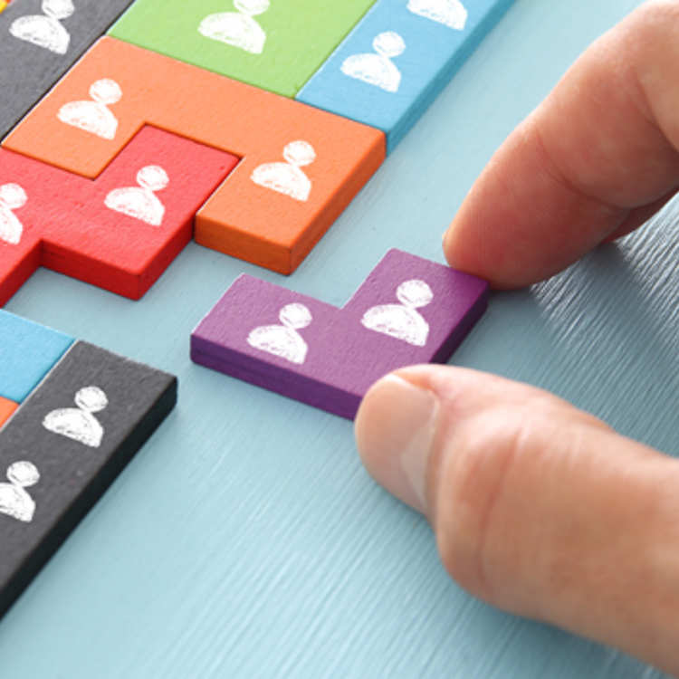 A hand places the final missing piece of a puzzle featuring symbols of people