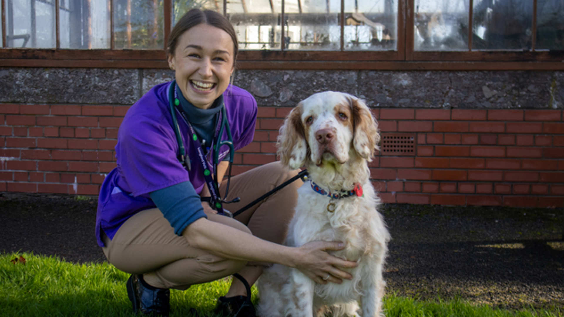 A smiling vet crouches next to a patient whilst exercising in the gardens