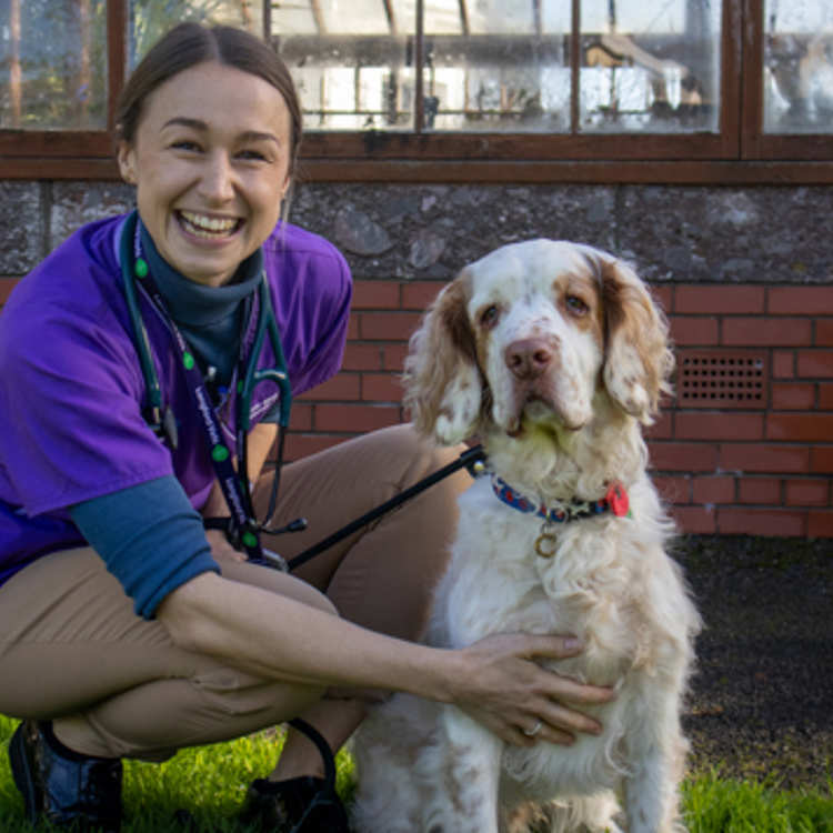 A smiling vet crouches next to a patient whilst exercising in the gardens